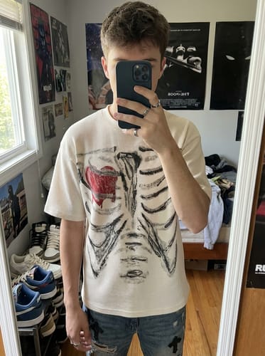 Reviewer in a mirror selfie wearing the cream Skeleton & Melted Heart Graphic Waffle Knit T-Shirt, showing the front print.
