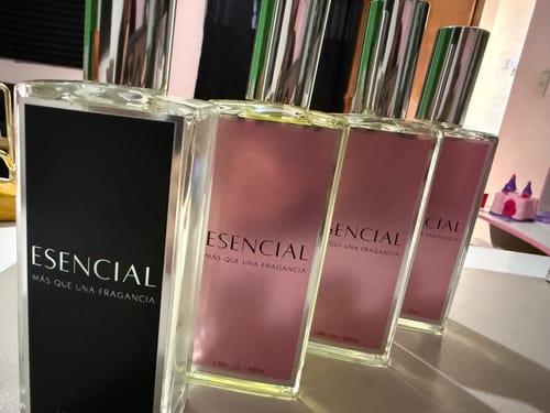 Un cliente muestra cuatro frascos de perfume de vidrio Esencial alineados sobre una superficie.