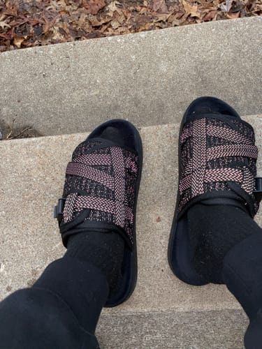 Customer wearing black Reflective DracoSlides with pink patterned straps and black socks on concrete steps.