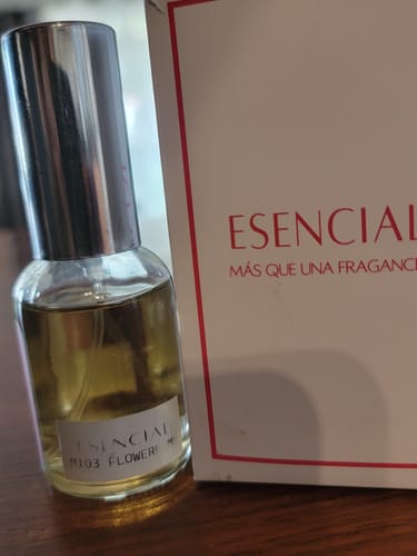 Cliente muestra el frasco del perfume Esencial M103 junto a su caja blanca con detalles rojos.