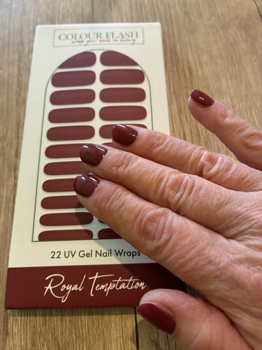 Hand einer Kundin mit aufgetragenen „Royal Temptation“ UV-Gel-Nagelfolien neben der Produktverpackung.