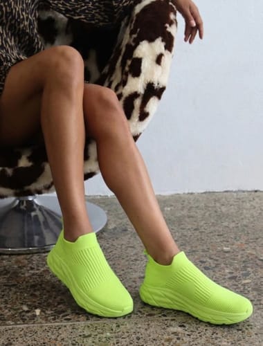 Reviewer sitting down while wearing a pair of bright neon-green Ortho Slip shoes.