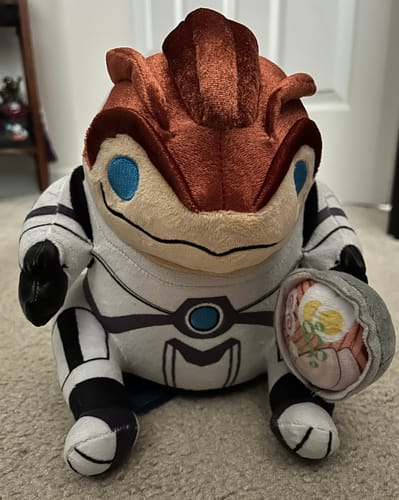Customer's Grunt Collector's Plush sitting on a carpet, holding a plush bowl of ramen in its hand.