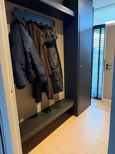 Recensent toont de zwarte Tumulo Large kapstok in een moderne hal, met jassen eraan.