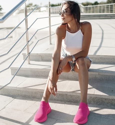 Customer sitting on outdoor steps wearing sleek, bright pink Ortho Slip shoes with a casual outfit.