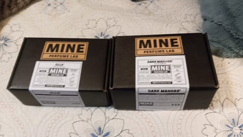 Recensore mostra le due scatole nere dei profumi, inclusa quella di OLLA', appoggiate su un letto.