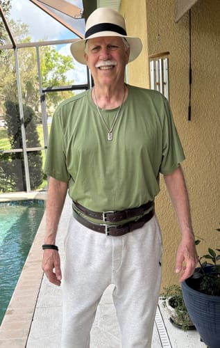 Reviewer smiling while wearing two of the brand's dark leather belts stacked over his shirt outdoors.