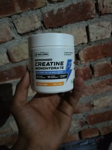 Customer holding a white tub of Wellcore Micronised Creatine Monohydrate in front of a brick wall.