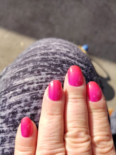 Hand einer Kundin, die ihre leuchtend pinken Nägel mit dem UV-Gel 'Hot Ombré' zeigt.