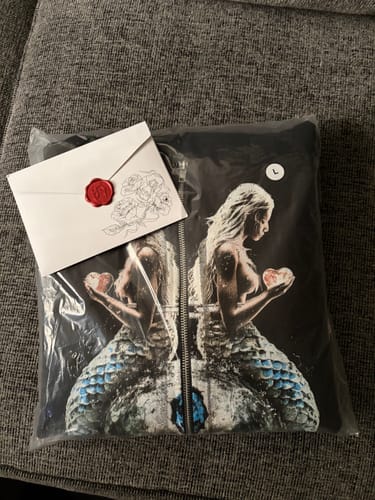 Reviewer shows the packaging from their purchase: a printed bag holding a hoodie and an envelope with a wax seal.