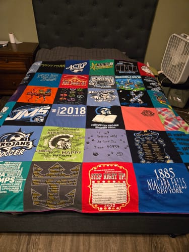 Customer's colorful Project Repat T-Shirt Quilt with custom patches laid out on a bed in a bedroom.