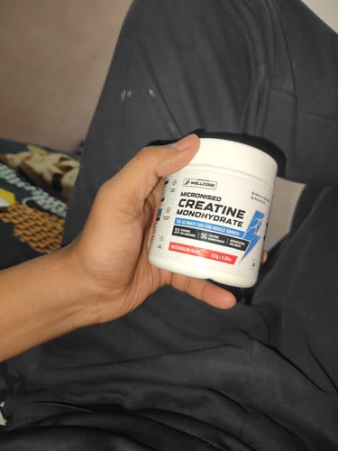A customer holding a white tub of Wellcore Micronised Creatine Monohydrate in Watermelon Wave flavor.