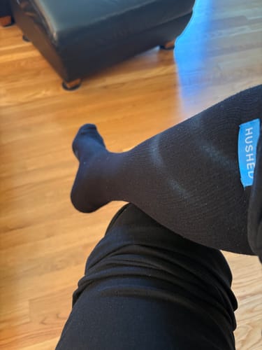 Customer sitting with their leg crossed, showing the fit of the black compression socks on their calf.