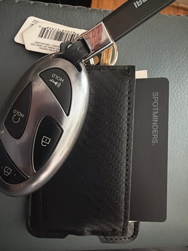 Customer's black SPOTMINDERS Tracking Card partially inserted into a black wallet, lying next to a car key fob.