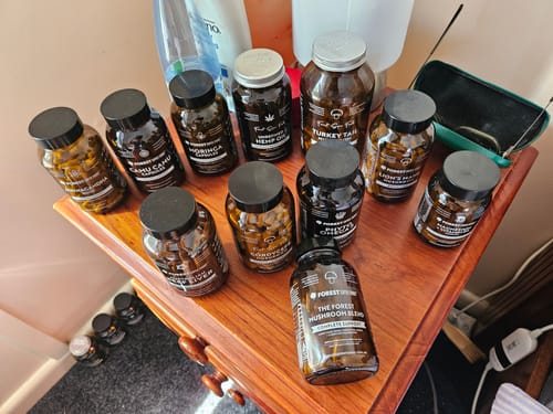 Customer's bottle of Organic Moringa Capsules on a wooden table with their large collection of other supplements.