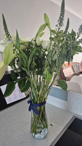 Customer's bouquet of tall white flowers and lilies in a clear glass vase on a kitchen counter.