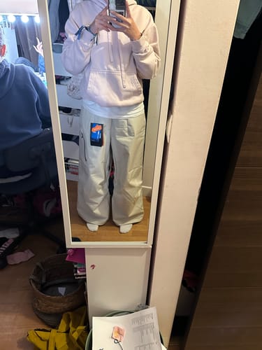 Reviewer in a mirror selfie wearing the baggy, off-white snow pants to show their oversized fit.