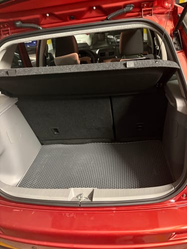 Recenzent prezentuje szarą matę do bagażnika z wzorem w romby, dopasowaną do wnętrza czerwonego auta.