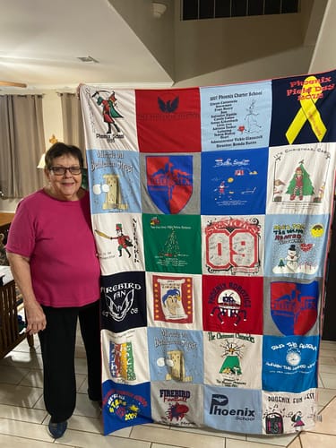 Customer smiling and standing next to her large Premium T Shirt Quilt made from many colorful school shirts.
