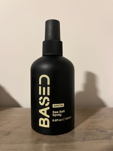 Customer's matte black bottle of Based Sea Salt Spray sitting on a wooden surface.