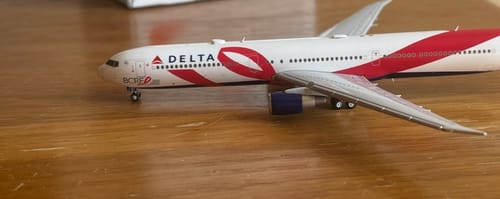 Reviewer's Gemini Delta 767-400ER model plane on a wooden table, showing its red breast cancer research livery.