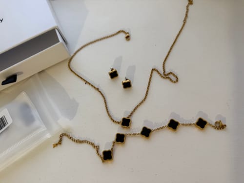 Reviewer's gold-colored jewelry set, including a necklace, bracelet, and earrings with black clover charms, laid out on a white surface.