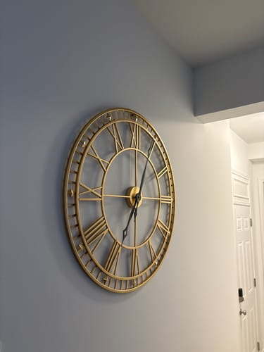 Customer's large Gold Roman Numeral Metal Wall Clock hanging on a light gray interior wall.