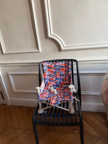 Reviewer's colorful floral Willow baby chair shown as a booster seat on a black chair indoors.