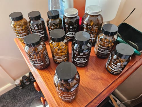 Customer's bottle of Unfiltered Hemp Seed Oil Capsules arranged with other supplements on a wooden table.