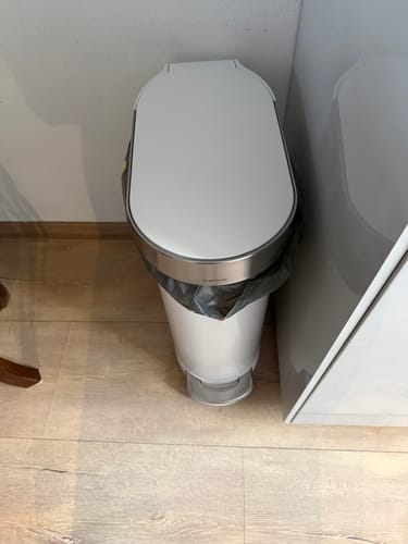 Recensent toont de witte Simplehuman Slimline pedaalemmer in een smalle ruimte.