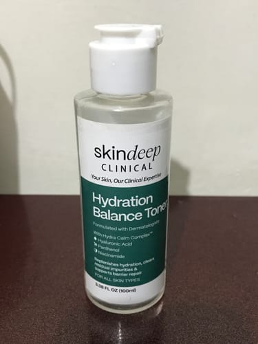 Customer's bottle of Hydration Balance Toner with a green and white label on a dark wooden table.