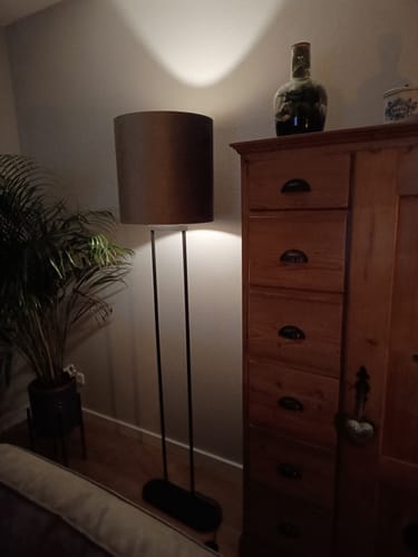 Recensent toont de brandende Thijmen vloerlamp met zwarte voet in een woonkamer naast een houten kast.