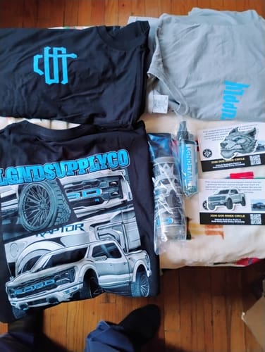 Customer displays the contents of their LGND89 Mystery CASH Box, including three shirts, two sprays, and two decals laid out.