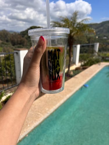 Cliente sujetando un vaso transparente con una bebida de matcha junto a una piscina.