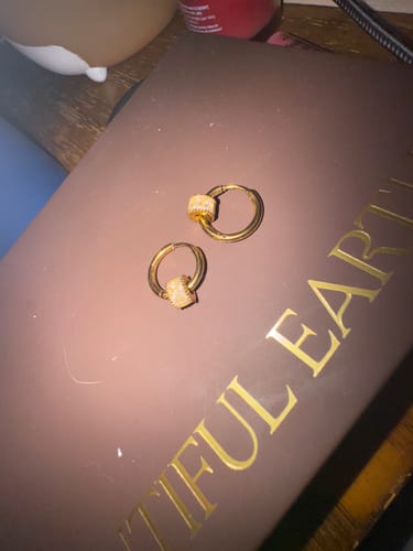 A reviewer's pair of Gigi Crystal 18K Gold Hoop Earrings resting on a brown box with gold lettering.