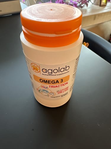 Recensore mostra il barattolo bianco di Omega 3 con tappo arancione su una scrivania.