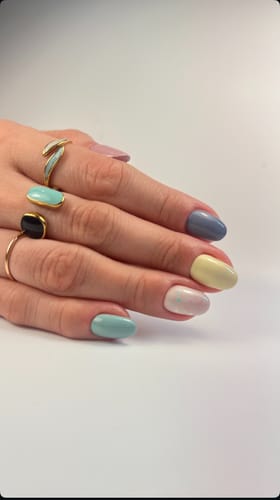 Customer's hand showing the gold Aquamarine Wrap Ring on the index finger, worn with other rings and a pastel manicure.