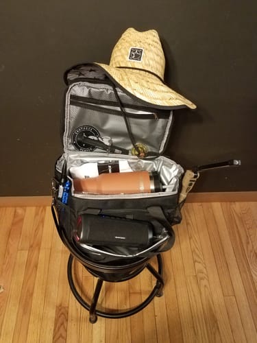 Customer's black lunch box shown open and full, containing a bottle, speaker, and other items on a stool.