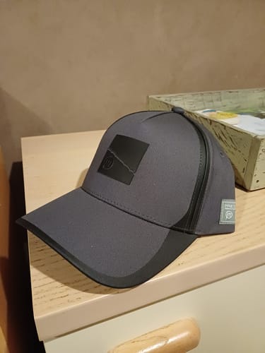 Recensent toont de donkergrijze en zwarte CORE COLLECTION CAP op een meubelstuk.