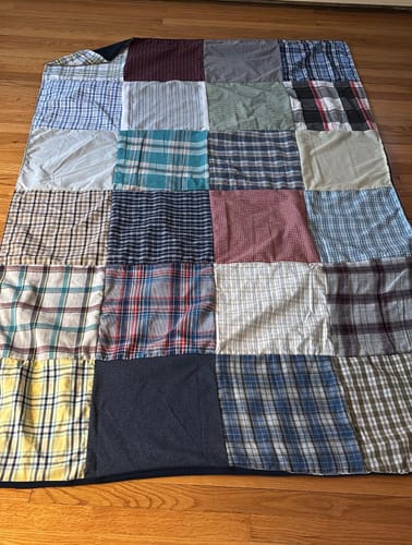 Customer's Premium T-Shirt Quilt made from various plaid and solid-colored shirts spread on a wood floor.