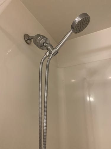 Reviewer's stainless steel handheld shower head and inline filter installed in their shower.