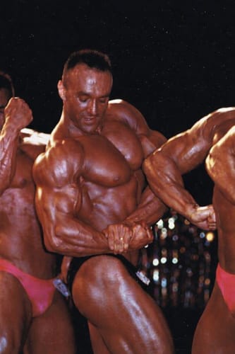 Recensore in posa da bodybuilding che mostra un fisico muscoloso e definito.