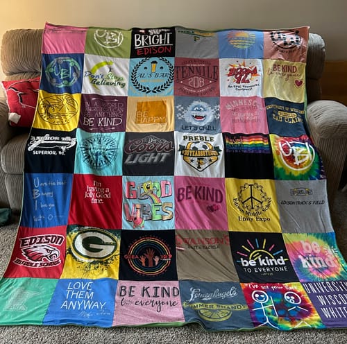 Customer's large, colorful Project Repat T-Shirt Quilt made from dozens of t-shirts, draped over a sofa.