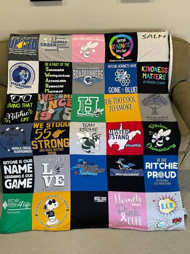 Reviewer's colorful Project Repat T-Shirt Quilt made from their school t-shirts, draped over a sofa.