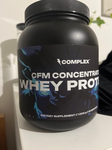 Reviewer's black tub of CFM Whey Protein sitting on a white shelf.