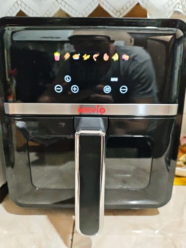 Clientul arată friteuza Air Fryer Novio StonePro neagră, cu panoul digital tactil pornit, afișând pictogramele de gătit.