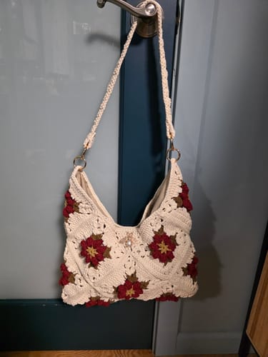 Reviewer's finished CrochetPark™ Garden Rose Hobo bag in cream with red flowers, hanging from a doorknob.