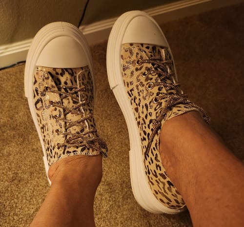 A reviewer's feet wearing the Aman Leopard Sneakers with white platform soles and sparkly gold laces.