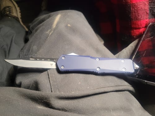 Customer's automatic knife with a blue handle and silver blade shown resting on their lap.
