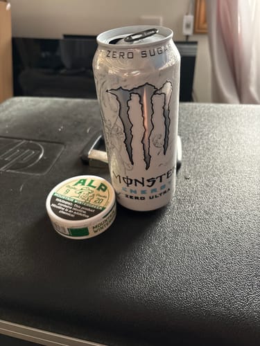 Customer's can of ALP Mountain Wintergreen Nicotine Pouches on a black surface next to an energy drink can.